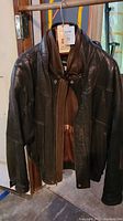 Black Pelle Studio men's leather jacket hanging on rack, visible front with zip and snap button closure, showing good condition with no visible damage.
