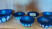 All six bowls displayed together on shelf, one large bowl at left and five smaller bowls in front.
