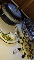 Photo showing the blue handmade bean pot with lid, Italian mixing bowl with blue and white mottled pattern, and floral ceramic sun and moon wall decor pieces.