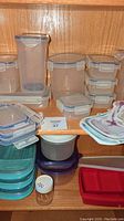 Assorted reusable kitchen containers including Lock & Lock in various sizes with blue locking lids, Rubbermaid divided containers, and reusable zip lock bags on a wooden shelf.