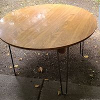 Round wooden table top with a waterproof laminate surface and attached hairpin legs placed on outdoor ground.