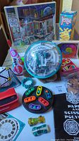 Photo shows multiple toys and games including a ViewMaster, Jenga box, unopened puzzle, UNO game, Sumoku puzzle, Perplexus maze ball, and other puzzles and small toys.