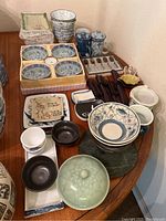 Overview of the full collection of Asian bowls, dishes, cups, containers, and utensils arranged on a wooden surface.