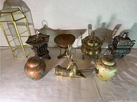 Photo of brass and metal collection items including incense burners, deer figurine, tripod bowl and two ceramic jars.
