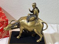 Side view of the brass figurine showing the seated rider on the ox mounted on a black felt base, illustrating the overall sculpture's size and form.