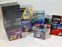 Various DVD and CD jewel cases in stacked sets including new sealed 25 and 50 count packages, plus a Fellowes branded DVD organizer box.