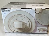 Original boxed packaging of JC Penney Home Collection Palladian 65-piece dinnerware set showing the stacked plates and cup with handle in soft cream color with gold accent rims.