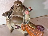 Front angle view of the ceramic Buddha statue showing the full body, facial features, and detailed colors and textures including the peach and orange cloth.