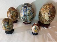 Front view of all five porcelain eggs together showing size differences, designs, and wooden stands.