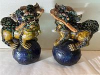 Front view of pair of Foo Dog statuettes showing their poses on blue spherical bases with detailed glaze and colors.