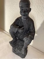Front angled view of the dark plaster statue showing sitting man with raised knee and arm resting on knee.