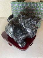 Front angle of black stone dragon turtle statue on wooden stand with patterned box behind.
