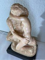 Side angled view of the nude embracing figures in the sculpture showing the detail of the male figure’s upper body and the female figure’s back and hair.