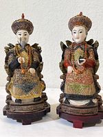Both Chinese man and woman ceramic figurines seated on carved chairs, showing detailed robes and headdresses