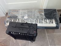 Overview of Casio XW-P1 keyboard wrapped in plastic with accompanying black amplifier