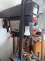 Front angle view of large gray and black Craftsman drill press with motor, control panel, control levers, and instruction decal on front panel.