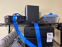 Photo showing electronic equipment including black speaker or subwoofer, power cords, and accessories on a metal rack.