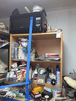 Shelf with black Westinghouse microwave, art supplies, bottles, and hardware items