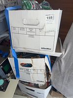 Three stacked OfficeMax boxes sealed with blue tape, containing various household hardware items inside.