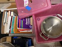 Boxes containing assorted books and pink plastic storage bin holding double boiler pot parts.