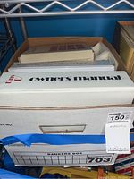 Top view of a box labeled 'owners manual' with visible Apple logo and other printed manuals inside a Bankers Box.