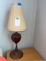 Full view of 28 inch table lamp with pleated cream shade and red glass or ceramic base on wooden platform
