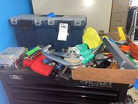 Overview of toolbox exterior with tools on top and a brown box with grips and other hand tool parts.