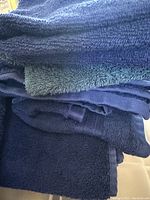 Stack of towels showing dark blue and navy bath towels and hand towels, made of terry cloth fabric.