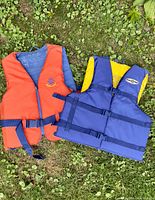 Photo showing the orange and blue/yellow lifejackets laid on grass, showing front and adjustable straps.