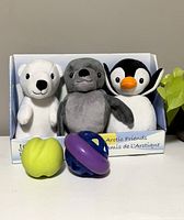 Front view of 3 plush dog toys (polar bear, seal, penguin) and 2 rubber chew toys (green apple shape, purple/blue ball) displayed in box