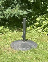 Photo showing full view of large circular heavy umbrella base on grass with central pole and securing screws visible.