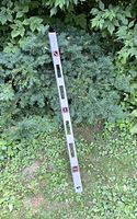 48-inch long metal level tool resting on grass and greenery, showing its length, rectangular shape, and multiple bubble vial windows with red accents.