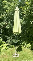 Photo showing the green outdoor umbrella closed and standing upright, surrounded by greenery.