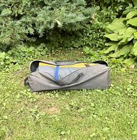 Gray outdoor tent carrying bag placed on grass, fully zipped and closed