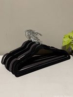 Set of black velvet hangers stacked and showing their profile shape and hooks.