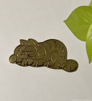Top view of the brass keyring shaped like a sleeping Garfield cat, showing the engraved cartoon details on the surface.