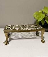 Front view of vintage brass rectangular plant stand with claw feet and ornate openwork design.