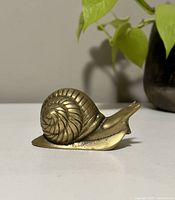 Side view of the brass snail figurine showing its coiled shell detail and smooth body with patina.