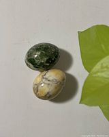 Two polished marble eggs displayed together on a white surface with a nearby green-leafed plant.