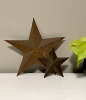 Front-facing image of two rusted metal star wall decor pieces on white surface, showing size contrast and rusty textured details.