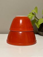 Stacked view of two vintage red Pyrex mixing bowls, showing their exterior red color and size difference.