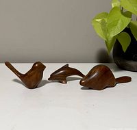 Photo showing three vintage handmade carved wooden animal figurines: bird, dolphin, and beaver, placed in a row on a white surface with a plant in background.