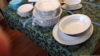 Photo of the stacked fine china set on table with bowls, plates, and saucers visible.