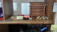 Image showing multiple necklace and bracelet pieces of costume jewelry laid out on a wooden surface with a tall wooden jewelry box in the background.