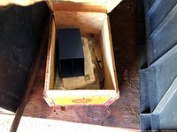 Empty wooden crate with a dark blue divider and papers inside, possibly for organizing small parts or tools.