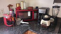 Full view of kitchen counter with red microwave, coffee makers, electric juicer, blender, and kitchen utensils.
