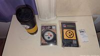 Photo of a Pittsburgh Steelers travel mug, two coaster sets, and a tag on a white surface.