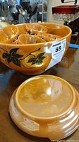 Photo showing amber-gold lusterware punch bowl with black leaf accents and several cups inside it.