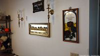 Wall display showing pair of brass sconces, Last Supper panel, and stained glass plaque hanging vertically