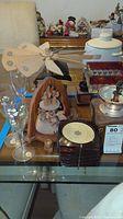 Overview of lot showing coffee grinder, wooden angel figurines, stemware, and coasters on glass table.